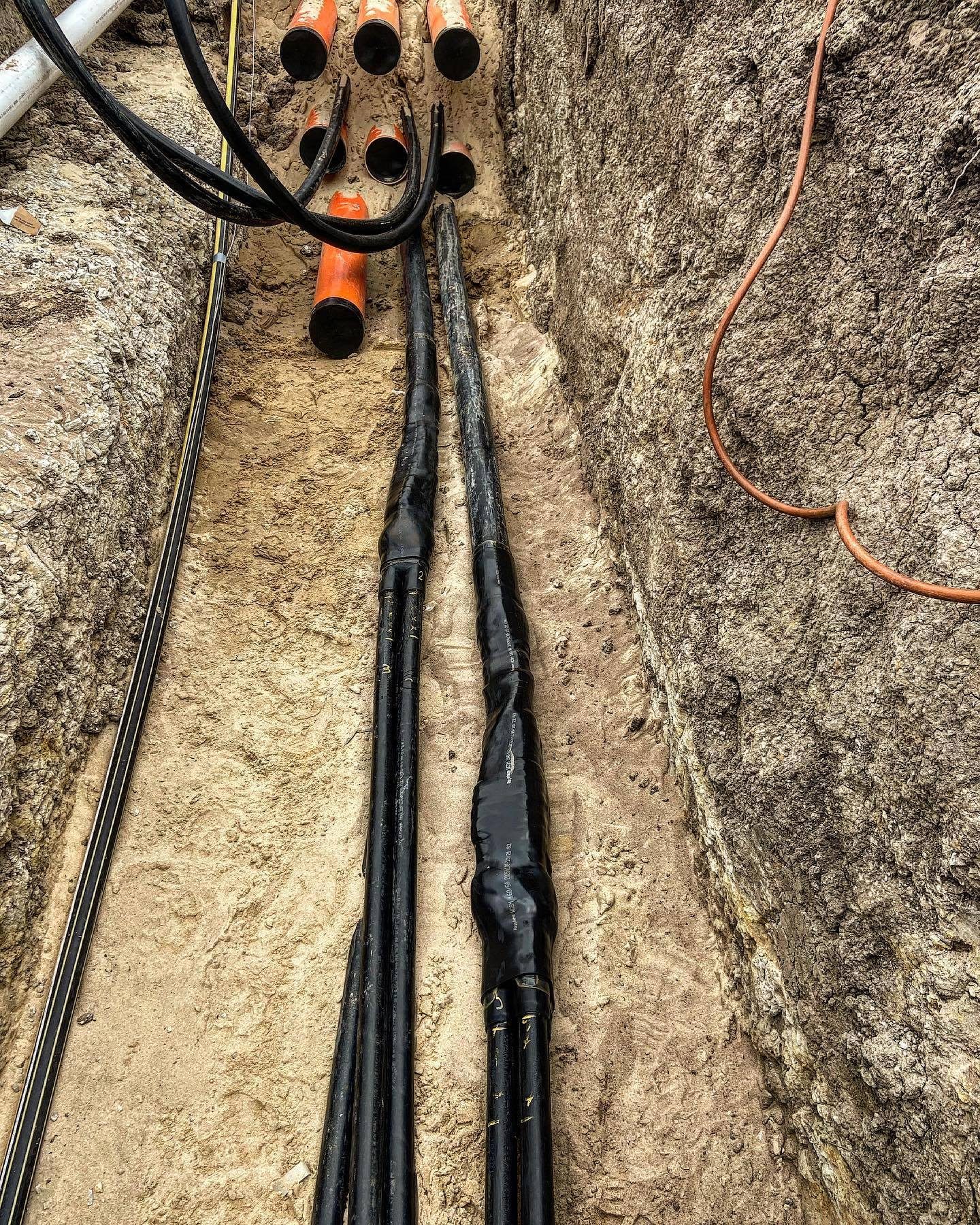 Underground consumer mains laid in an open trench alongside orange conduit