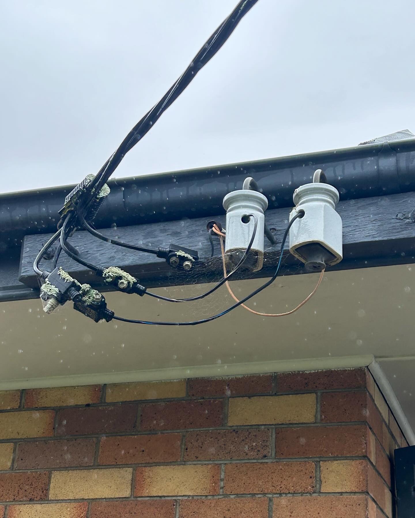 Old porcelain insulators and tangled service cables at a point of attachment on a brick house